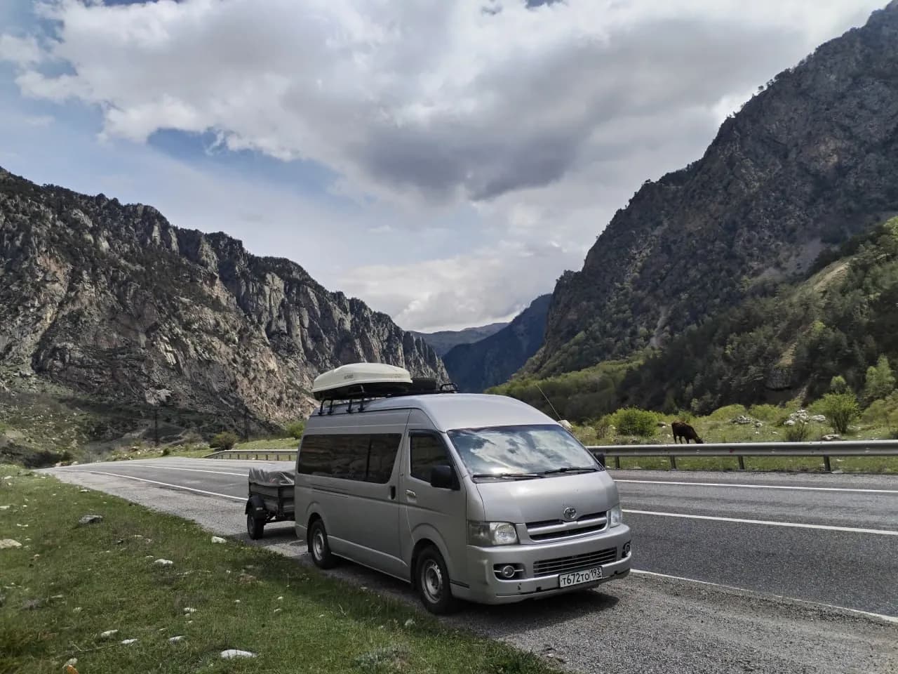 Микроавтобус Toyota Hiace с прицепом на горной дороге в каньоне Кавказа